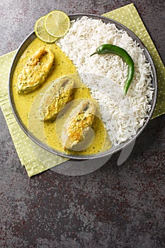 Illish or Hilsa fish cooking with mustard seed sauce served with white rice closeup on the plate. Vertical top view