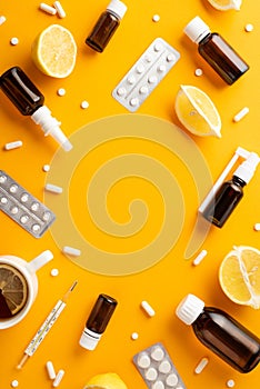 Illness concept. Top view vertical photo of remedy spray and syrup bottles pills blisters thermometer cut lemon and cup of tea on