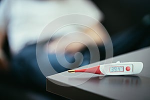 Illness and fever: Thermometer and ill man lying on the sofa in the blurry background