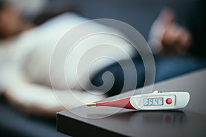 Illness and fever: Thermometer and ill man lying on the sofa in the blurry background