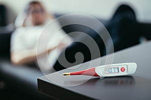 Illness and fever: Thermometer and ill man lying on the sofa in the blurry background