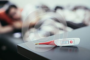 Illness and fever: Thermometer and ill man lying on the sofa in the blurry background