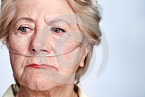 Illness and regret. Closeup of a sickly senior woman wearing a nasal cannula for oxygen isolated on blue - Copyspace.