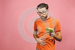 Illness sad young man in casual put hand on pain abdomen, stomach-ache, standing and holding burger isolated on pinke background.