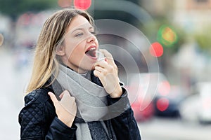 Illness young woman using a analgesic spray to soften the throat in the street.