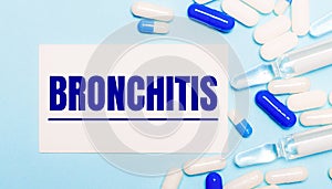 Ills, ampoules and a white card with the text BRONCHITIS on a light blue background. Medical concept