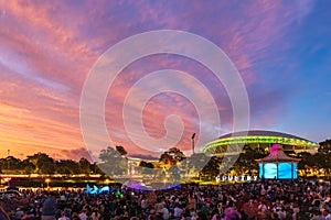 Illuminated Adelaide Oval under spectacular sunset clouds with people