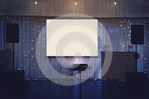Illuminated banquette hall stage with a big white screen and acoustic systems. Equipment for video and audio projection at a festi