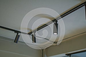 Illuminated black track light on ceiling. Modern LED Hanging rotating spot light.