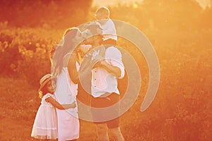 Illuminated bu sunlight. Family of four people spending free time on the field at day time of summer