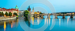 Illuminated Charles Bridge reflected in Vltava River. Evening panorama of Prague, Czech Republic. Panoramic shot