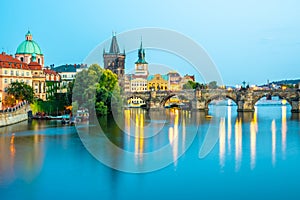 Illuminated Charles Bridge reflected in Vltava River. Evening panorama of Prague, Czech Republic. Panoramic shot