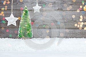 Illuminated christmas tree on snow and white stars against grey