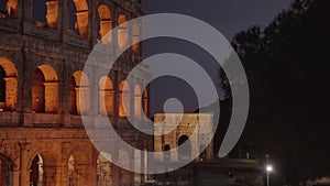 Illuminated Colosseum by triumphal arch in Rome at twilight