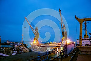 Illuminated floating dock in shipyard at night. Vessel maintenance underway with cranes and lights. Maritime industry