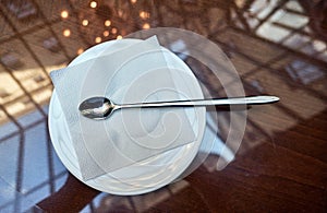 Illuminated glass restaurant roof reflecting in glassy table surface and polished stainless steel spoon on white paper towel