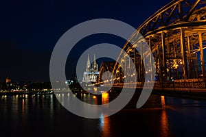Illuminated Hohenzollern Arch Bridge and a historic ancient cathedral in Cologne, Germany at night
