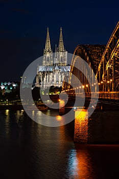 Illuminated Hohenzollern Arch Bridge and a historic ancient cathedral in Cologne, Germany at night