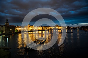 Illuminated Moldova River With Ship And Historic Buildings In The Night In Prague In The Czech Republic