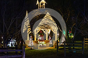 Illuminated Night View Of Small Chapel Surrounded By Multiple Christmas Trees Decorated With Lights