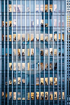 Illuminated office of an high-rise building facade with people working inside. Modern business buildings, banks and office