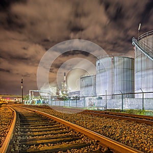 Night scene with illuminated petrochemical production with large silos and rails