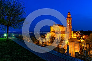 Illuminated parish church under blue morning sky in small italian town.