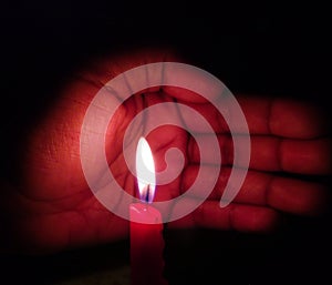 Illuminated Red candle protected by hand
