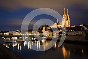 Illuminated saint Peter cathedral with historical stone bridge after dark in Regensburg, Bavaria, Germany. Cityscape image over