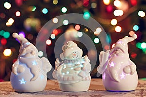 Illuminated Snowman and Jack Frost (Santa Claus) dolls in front of Christmas tree lights, blurred background