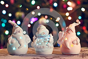 Illuminated Snowman and Jack Frost (Santa Claus) dolls in front of Christmas tree lights, blurred background