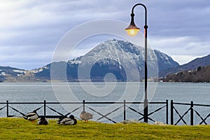 Illuminated Street Lamp Overlooking a Peaceful Lake Scene With Snow-Capped Mountain Background at Dusk