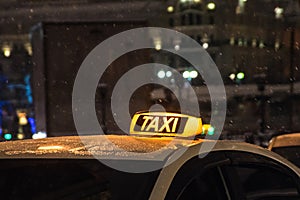 Illuminated taxi sign on the roof of a taxi at night city