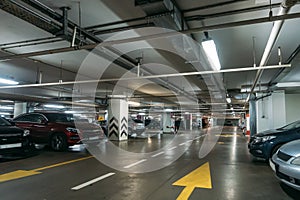 Illuminated underground car parking interior under modern mall with lots of vehicles and arrows on floor