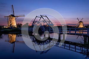 Illuminated windmills, a bridge and a canal at sunset