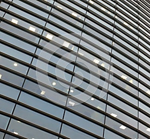 Illuminated windows on the facade of a large curved modern office building with lights turned on on at twilight