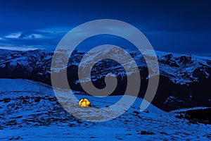 Illuminated yellow tent in a wintry blue cold landscape