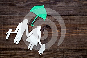 Illustration of social security concept. Financial protection. Family silhouette, cutout under umbrella on dark wooden