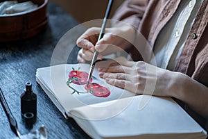 Illustrator designer student painting sketches tomatoes in sketchbook sitting at desk in art school.