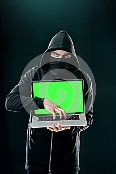 Im coming for your passwords. Portrait of a computer hacker using a laptop while standing against a dark background.