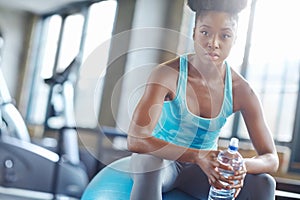 Im committed to fitness. an serious young woman holding a bottle of water while sitting on a pilates ball at gym.