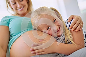 Im going to be the best big sister and babysitter. Portrait of a little girl hugging her mothers pregnant belly at home.
