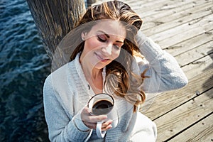 Im just going with the flow today. a beautiful young woman enjoying a warm beverage on a pier at a lake.