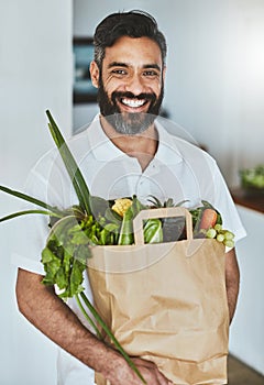 Im making an investment in my health. Portrait of a happy man holding a bag of fresh vegetables while standing in his