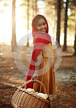 Im off to visit Grandma. Portrait of a little girl dressed in a red cape and holding a basket in the woods.