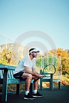 Im so prepared to win today. a sporty young man sitting on a bench on a tennis court.