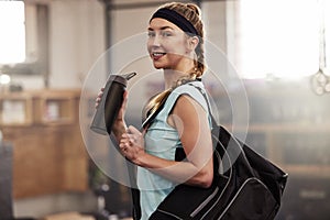 Im ready for my gym session. Shot of a young woman holding a water bottle and carrying her gym bag.