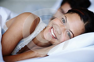 Im ready to face the new day. Smiling young woman lying in bed alongside her boyfriend.