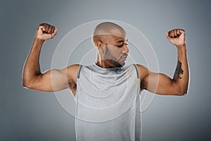 Im strong and thats enough. a sporty young man flexing his muscles against a grey background.