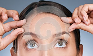 Im treading water I swear. a beautiful young woman checking her forehead against a blue background.